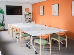 a meeting room with orange wall and a table and 12 seats set up for a meeting